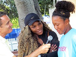 A reporter holding a microphone to Osaka with Williams to the side smiling