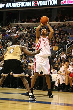 Howard is shooting a basketball over another Black athlete while an Asian athlete watches.