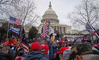 A crowd of people outside and inside of the United States Capitol Building. Many are wearing red hats and carrying United States flags.