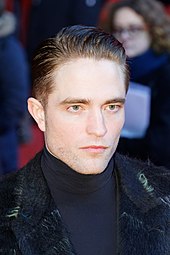 Pattinson with a stern look on his face looking towards a camera