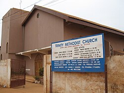A brown church with a gate and a sign reading "Trinity Methodist Church".