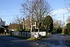 Street scene with area between two roads containing trees and stone column behind a white fence.