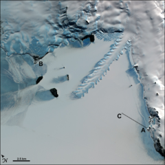 aerial view of a frozen bay, with a long peninsula of ice protruding from a snow-covered shoreline