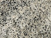 A closeup of the polished face of a slab of granite showing grains of white, bluish gray and black.