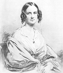 Three-quarter length portrait of woman aged about 30, with dark hair in centre parting straight on top, then falling in curls on each side; she smiles pleasantly and is wearing an open-necked blouse with a large shawl pulled over her arms