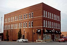 A three-story wall-to-wall building on a corner. The front windows have awnings featuring alternating News on 6 and KQCW logos.