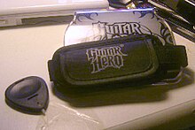 The "Guitar Grip", a hand-sized unit that fits into the Nintendo DS with four colored fret buttons on one end, and an adjustable strap that the player wears to hold the Grip and DS in place while playing. The Grip features the "Guitar Hero: On Tour" logo on one side.