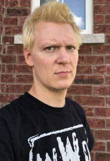 Aubrey Cottle, photographed from the shoulders up, standing in front of a brick wall