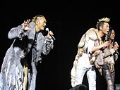 An image of three men looking over the crowd from the stage and singing into hand-held microphones