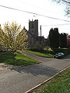 Stone building with square tower. In the foreground is a road.