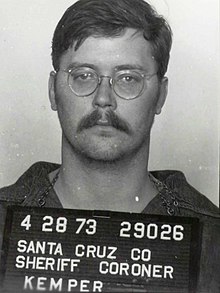 Black-and-white photo of an expressionless mustachioed man wearing owl-eye glasses