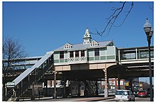 A green station house in a Queen Anne style, with a staircase on the left side leading up to it