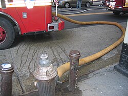 A New York City hydrant hooked to an FDNY fire engine with a fire hose actively pumping water