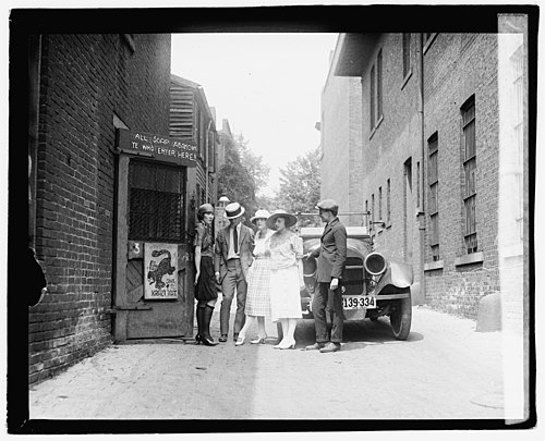 Gershwin's work has been cited by writers and scholars as embodying the Jazz Age's zeitgeist with its flappers and speakeasies. Above: Patrons and a flapper await the opening of a speakeasy in 1921.