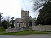 Stone building with square tower separated from the road in the foreground by a stone wall.