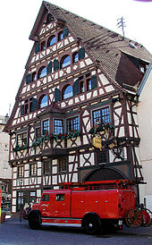 A colour photograph of a timber framed house with a red truck standing in front.