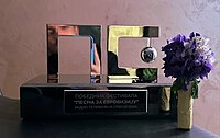 Trophy in the form of the Pesma za Evroviziju logo (cyrilic letters P, as well as S and E combined). On the pedestal it is written "Winner of Pesma za Evroviziju – Radio and Television of Serbia 2024. There is also a bouquet of flowers in the picture