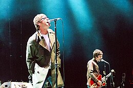 Oasis performing onstage, singing into microphones