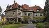 A large house of many windows with white panes, and with a red-checkered roof with many steep sides