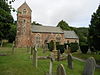 Stone building with square tower. In the foreground are gravestones.