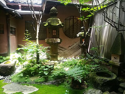 Straight-on view of the same garden. Note shitaji or renji windows, water basins, lanterns, and shade-loving plantings, including ferns, Soleirolia soleirolii, and a moss lawn.