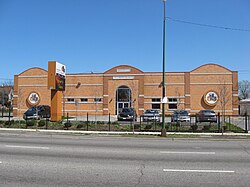 A large brick building behind black gates with and a parking lot with several parked cars