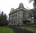 Photograph of Villard Hall, its imposing facade and mansards frost-rimed on a wet, cloudy winter day. A modern addition to the building is obscured behind a tree.