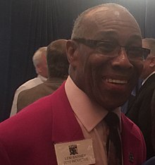 Lem Barney in a red suit jacket, shown from about the chest up and smiling.