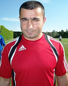 A man wearing a red t-shirt stands on field