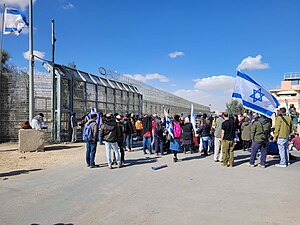 Protesters in front of a border gate blocking humanitarian aid trucks to the Gaza Strip at the Kerem Shalom Border Crossing, with one carrying an Israeli flag.