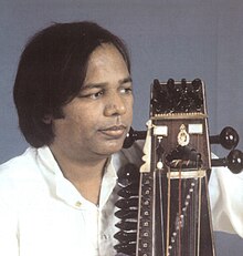 Narayan looks to the side with a sarangi held close to his body.