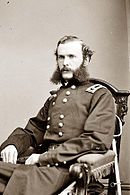 Photo of a seated man with large mutton chop beard wearing a dark military uniform with a general's shoulder tab.