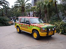 A utility car painted in green, yellow, and red colors in a jungle park environment.