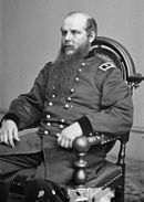 Photo shows a seated man in a dark military uniform with the two stars of a major general on his shoulder tab. He is balding and has a very long curly beard.