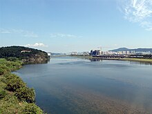 A vast and tranquil river in a clear day of fall. Apartment blocks and buildings under construction are seen at a distance.