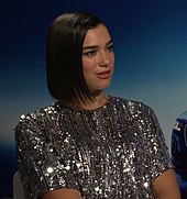 Dua Lipa wearing a glittery dress against a blue background