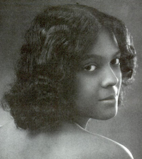 A young dark-skinned woman with dark wavy chin-length hair, looking over her bare shoulder