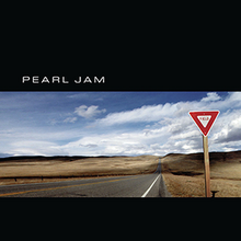 A triangular yield sign alongside a desertic road. Above and below the image are black bars, the top one having the text "Pearl Jam".